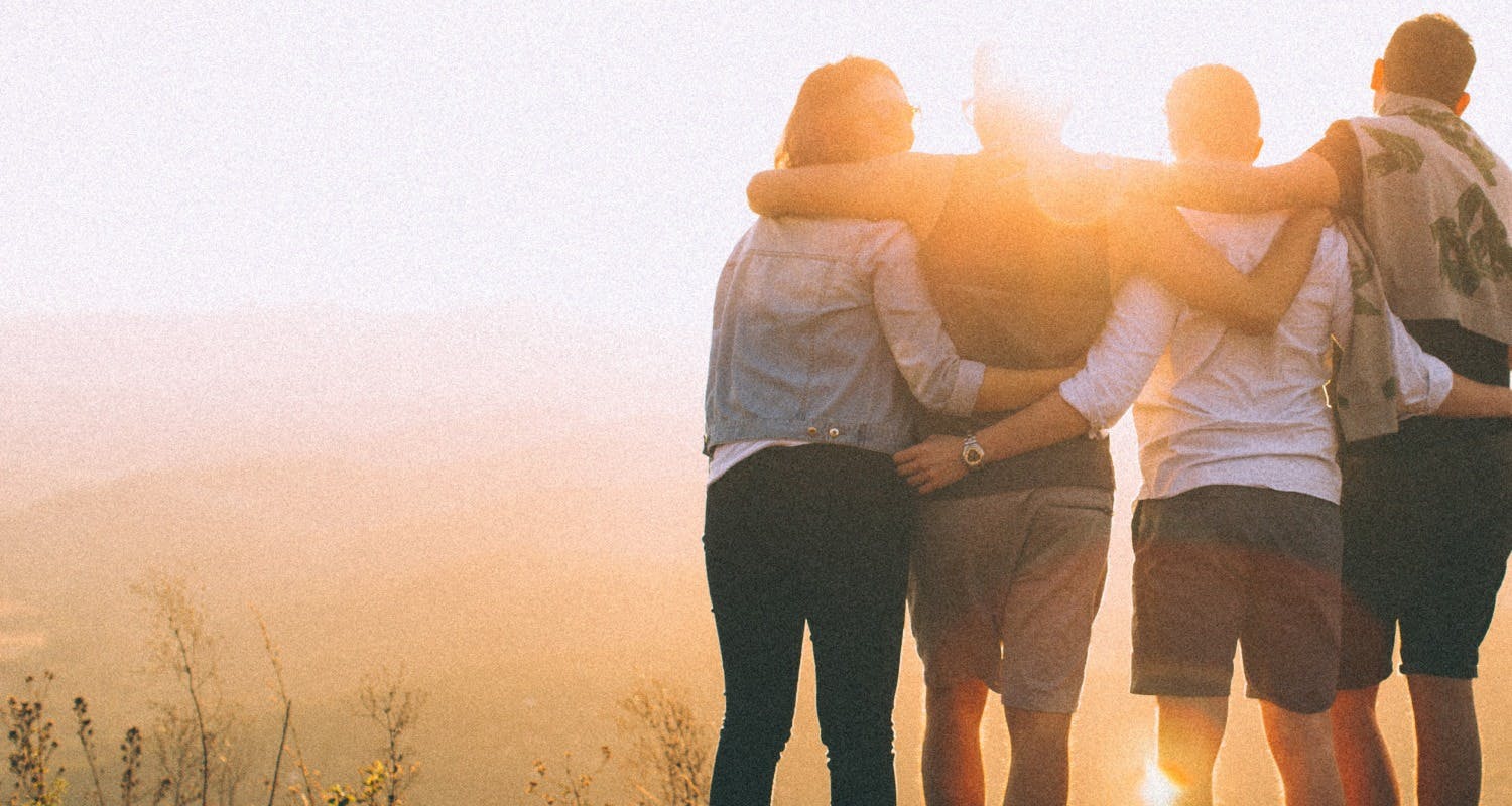 friends putting their arms around each other while watching the sunset