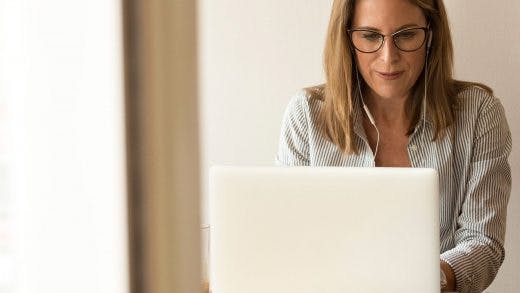 lady with headphones smiling while typing on her laptop