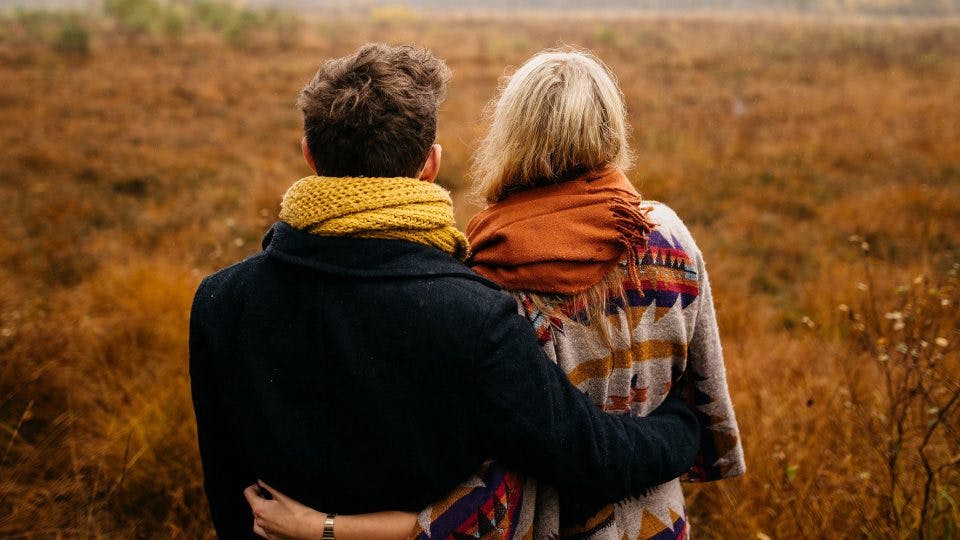 man and woman with their arms around each other looking at the grassy field