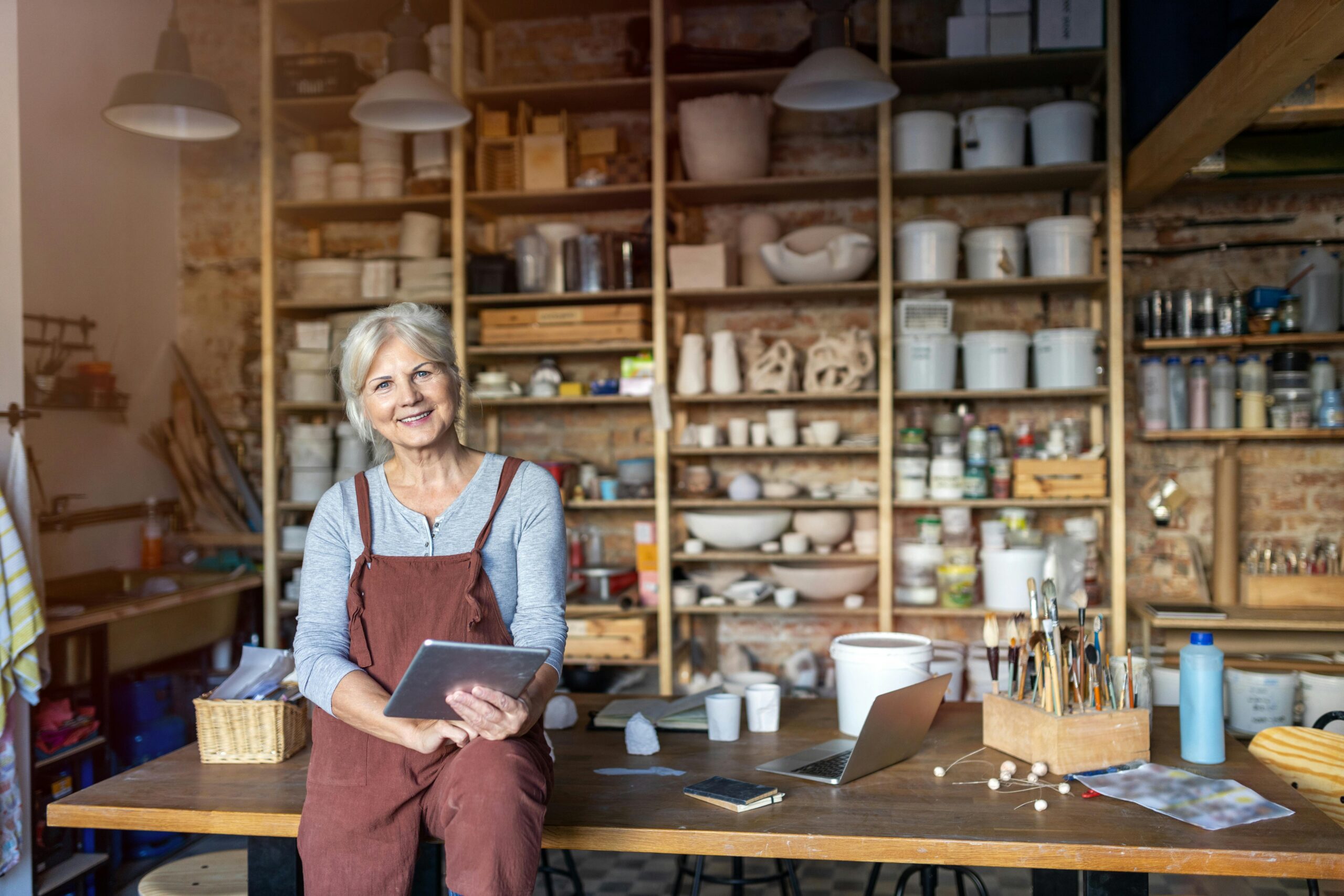 woman sitting on a table with a bunch of crafts holding an ipad