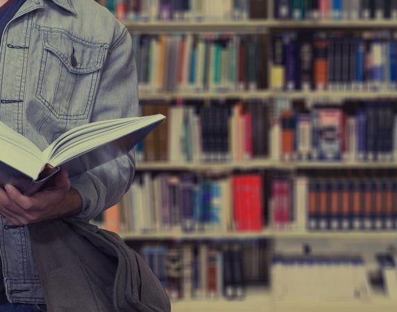 man holding a book in front of library shelf