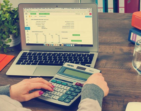 woman using calculator with her computer in the background