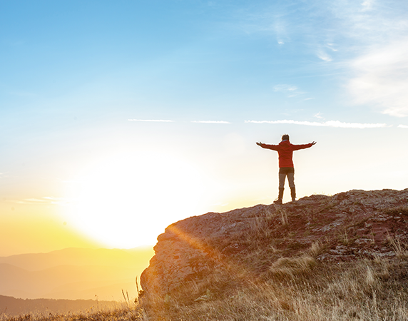 person on top of the mountain with their hands up enjoying the sunset view