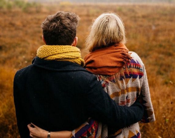 man and woman with their arms around each other looking at the grassy field